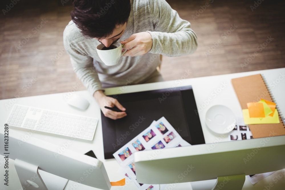Poster businessman having coffee while using graphics tablet