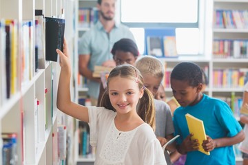 Smiling girl removing book from bookshelf in library 