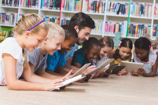 Teacher and kids lying on floor using digital tablet in library - Powered by Adobe
