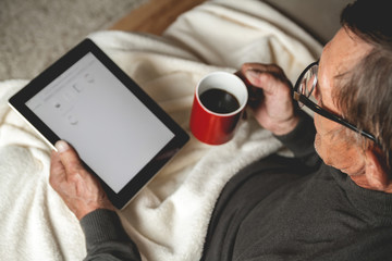 Senior with spectacled sitting on the couch with a tablet  and red cup of coffee in hands. Online education retirement concept. e-Learning. mock up