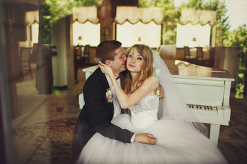Groom kisses bride's cheek and smiles sitting behind the piano