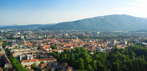 Fototapeta premium Pseudo aerial cityscape scenery of Maribor from Piramida Hill. City park, historical old town centre / center and Pohorje mountain. Summer season and yellow light of sunset