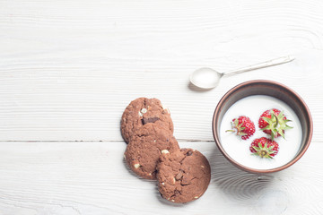 Fresh strawberries in bowl with cookies on white wooden table