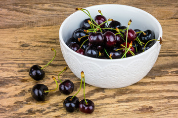 Red cherries in a white ceramic bowl on wooden background.