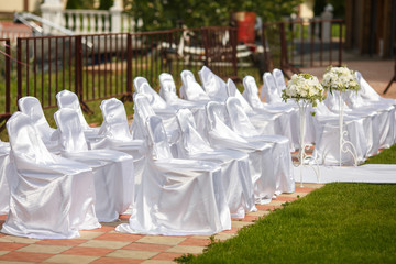 Chairs dressed in white satin wait for guests of a wedding