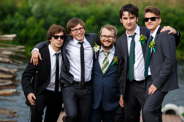 Stylish dressed groom and groomsmen pose together by the river