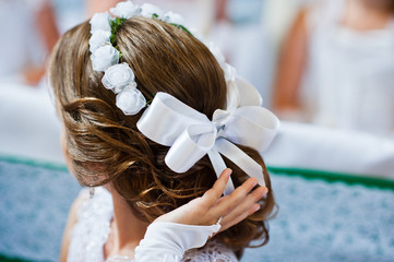 White bow and wreath on hairstyle of little girl on first holy c
