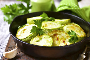 Fried zucchini in a skillet with spicy green sauce.