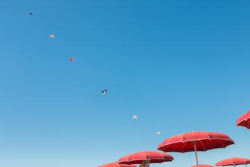 Spielzeugdrachen am blauen Himmel und rote Sonnenschirme
