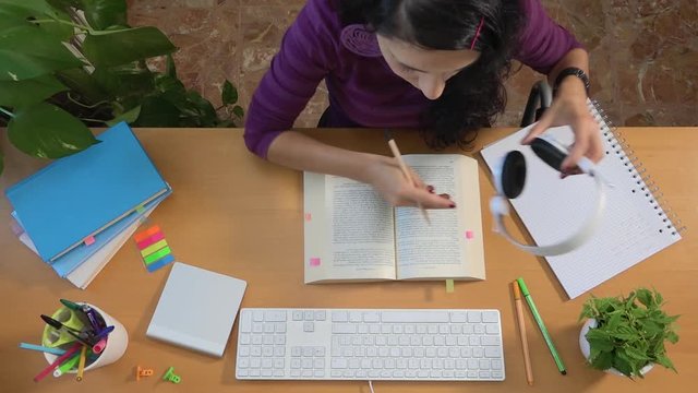 Female college student listening music and studying to preparing exam. Caucasian girl wearing headphones and reading a book. Studying for degree. Young people, university life and learning