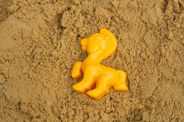 Plastic children toys for playing in sandpit or on a beach . Yellow horse .  A form for game with sand