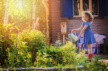 child girl watering flowers in summer garden, little helper, country rural scene