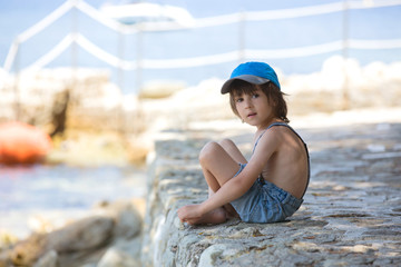 Cute boy, sitting on a pier in mediterranean sea on French rivie