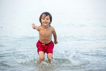 Cute boy, splashing water on the beach