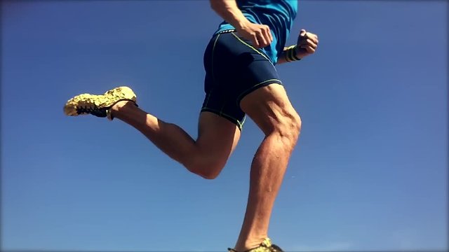 Athlete wearing gold shoes running across the bright blue sky in slow motion