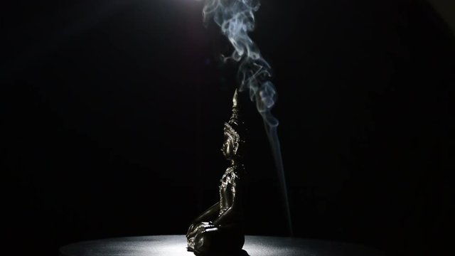Image of seated Buddha figure turning on black background with smoke