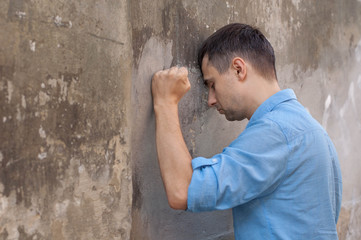 Fototapeta na wymiar Depression and hopelessness. Depressed young man leaning at the wall