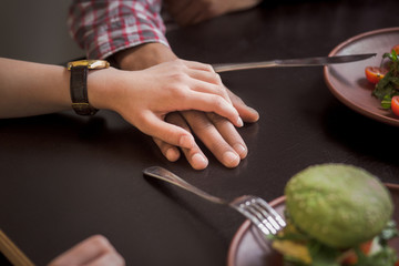 Happy couple eating vegan dishes in vegan restaurant or cafe. Closeup picture of man and woman holding each other's hands.