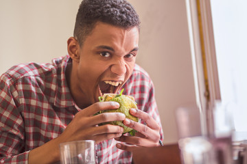 Portrait of hungry man eating vegan burger in vegan restaurant or cafe. Handsome man with short...