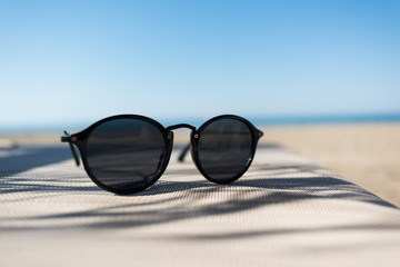 Female sunglasses on a sun lounger with defocused sand beach and sea on the background