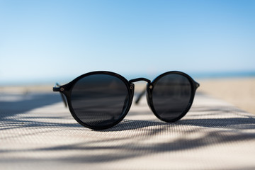 Fototapeta na wymiar Female sunglasses on a sun lounger with defocused sand beach and sea on the background