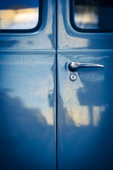 Ancient Van Door Detail / Closeup of locked blue oldtimer car back door with windows, lock and door handle in mysterious vintage light with reflections on it - 116253285