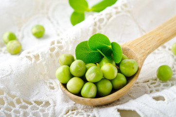 Fresh raw organic green peas in wooden spoon on white background