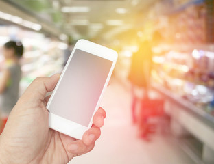 hand holding the smartphone on supermarket in blurry for backgro