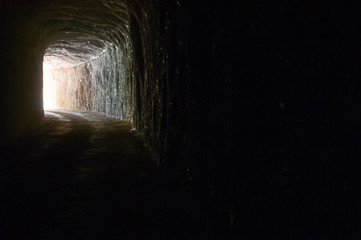Dark road in a natural rocky tunnel and the light of the exit