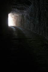 Dark road in a natural rocky tunnel and the light of the exit