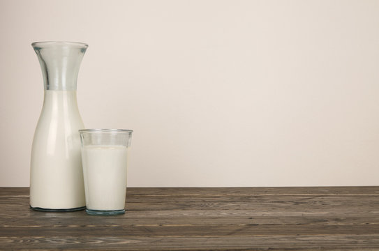 A vintage style glass bottle of milk and glass on a wooden table top background