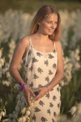 Fototapeta premium Princess. Young beautiful pretty woman posing in long evening luxury dress against bushes with white flowers