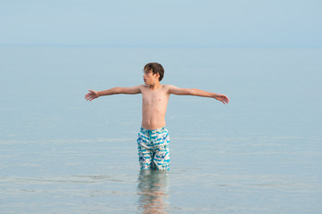 child standing in a calm lake with his arms outstretched