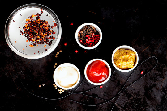 Spices - hot chili pepper, mustard, pepper - and sauces -white, mayoneese, spicy oil - on the black natural background 
