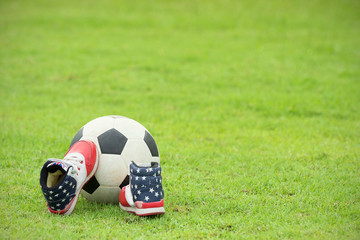 Close up of football with kid shoes in the field.
