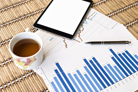 Tablet  and tea cup with financial documents on wooden table