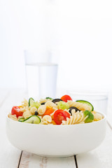 Pasta salad with vegetables on white wooden table