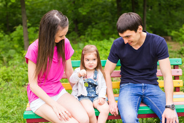 Fototapeta na wymiar young family sitting on a bench in the summer park