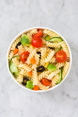 
Pasta salad in bowl with vegetables on white marble
