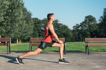 Fototapeta premium Fitness man stretching legs before outdoor workout. Sporty male athlete in an urban park warming up.