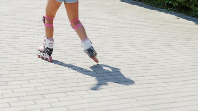Back of girl riding on roller skates. Slow Motion. / Back of girl in pink helmet riding on roller skates in summer park