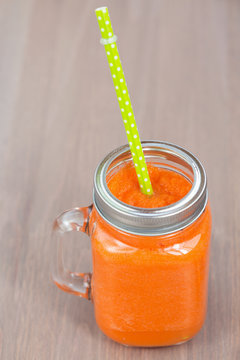 Healthy carrot smoothie in a jar with green tube on wooden background