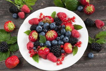 White plate with fresh berries on wood background