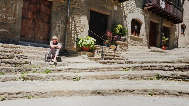Woman sits on the steps of the ancient town in Catalonia Rupit. A popular place among tourists