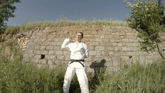 Man in white kimono trains with nunchaku background of wall