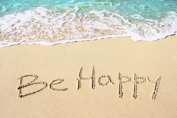Be happy handwritten with soft ocean wave on the sandy beach