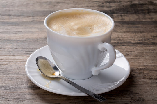 Cappuccino in weißer Tasse auf Holzhintergrund.