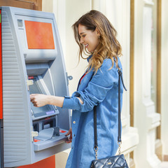 Fototapeta na wymiar Happy brunette woman withdrawing money from credit card at ATM