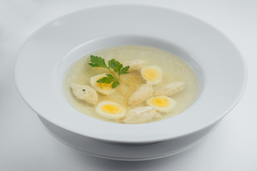 Chicken soup in a white plate with eggs and greens