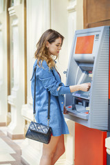 Happy brunette woman withdrawing money from credit card at ATM
